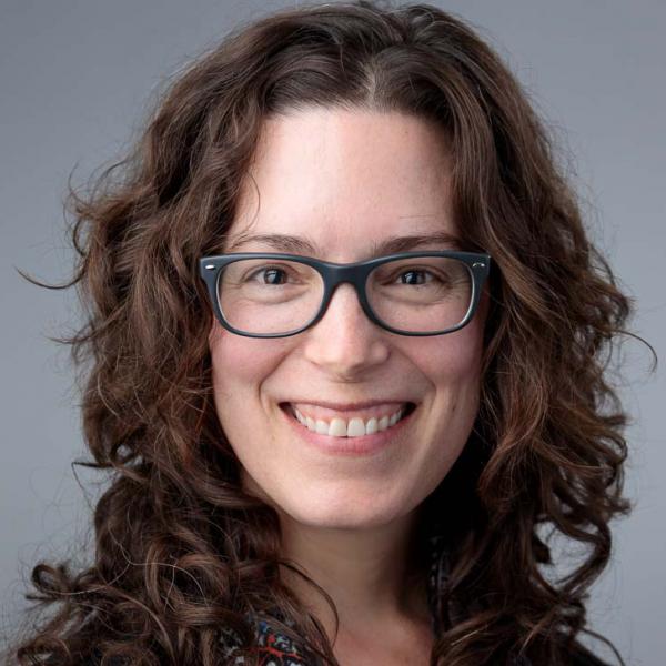 Photo of smiling white woman with shoulder length brown hair wearing black glasses