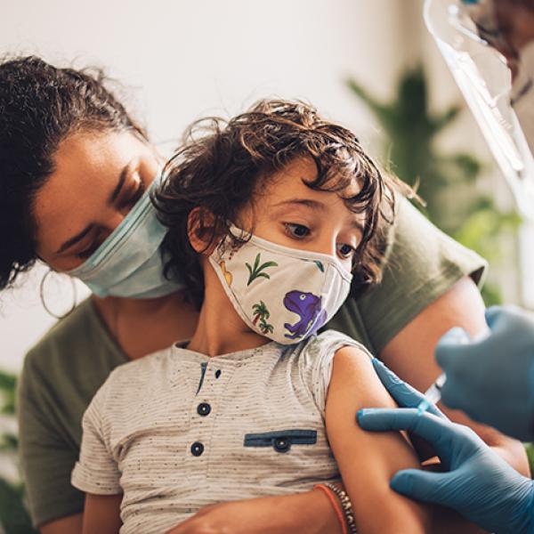 Masked child with brown curly hair getting COVID-19 vaccine shot