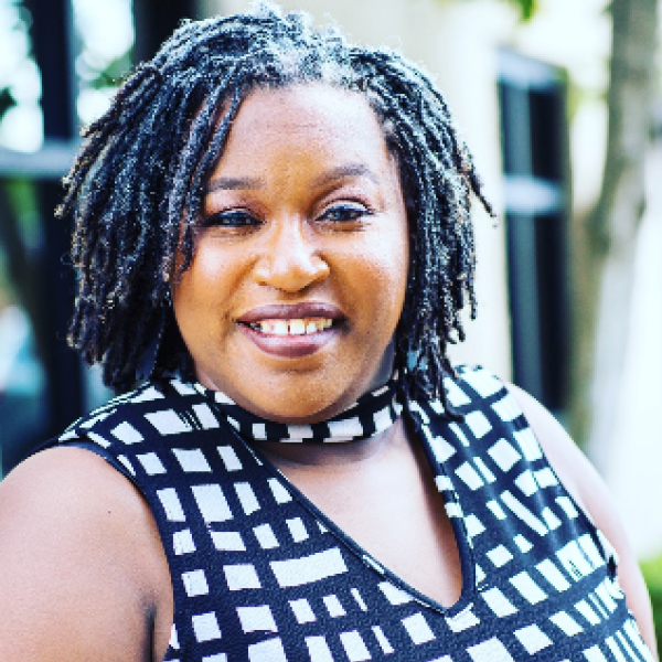 Smiling Black woman with shoulder length dreadlocks wearing a black and white patterned sleveless blouse