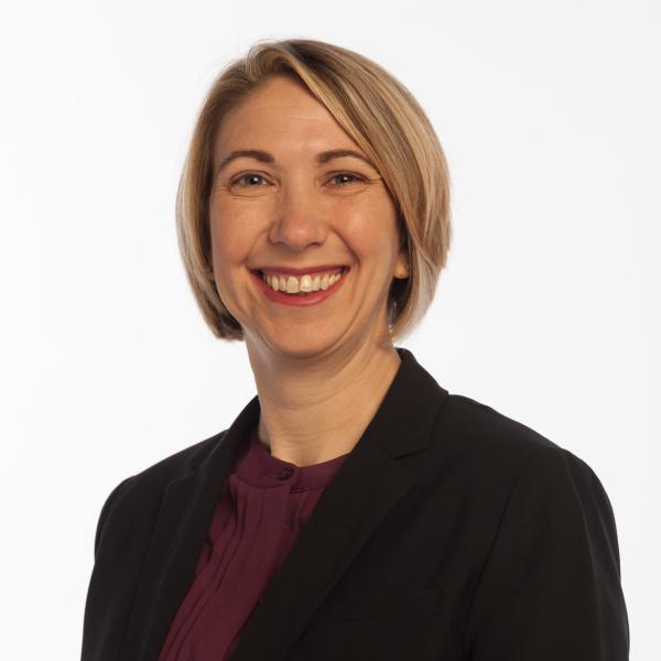 Smiling white woman with chin length straight blonde hair wearing a black blazer over a maroon blouse.