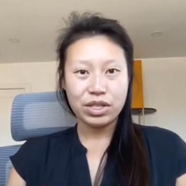 Asian woman with black hair wearing a black blouse sitting in an office chair speaking and looking straight ahead.